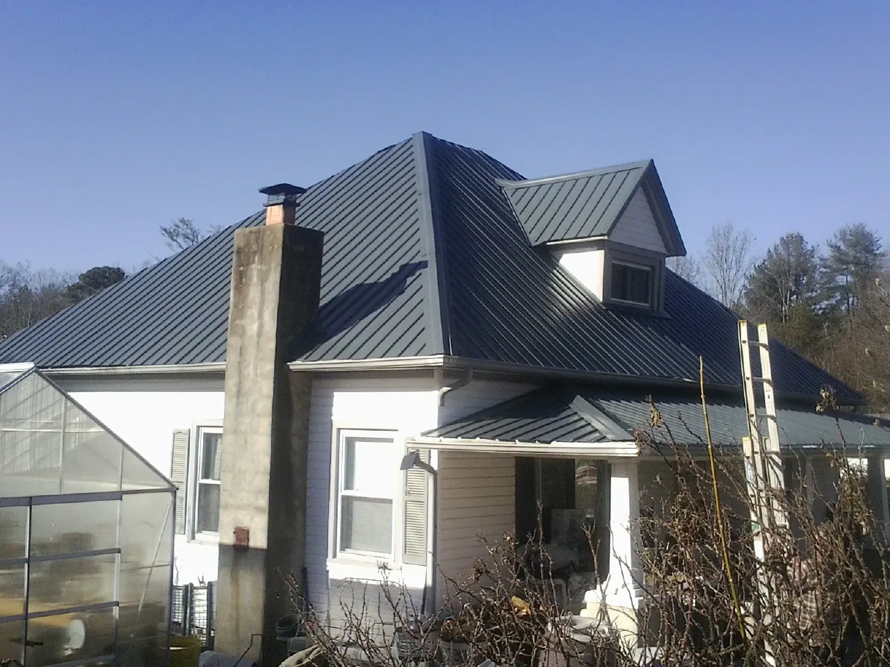 Dark blue standing seam metal roof on a white farmhouse with dormer — Slate & Tile Roof Repair by Roofing Brothers in Ida