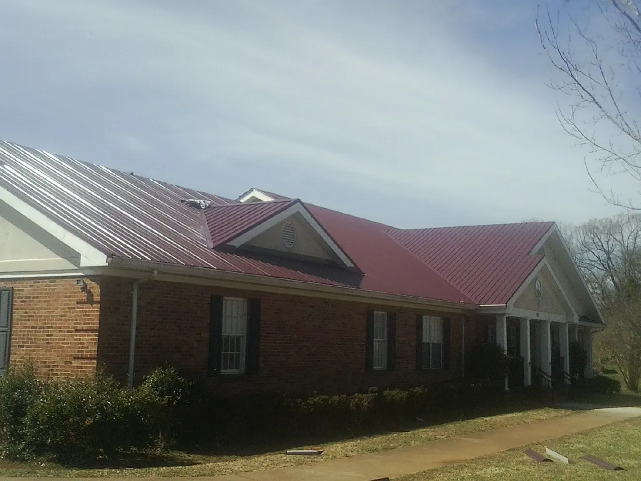 Red metal roof with gabled entries on a long brick building, from a Hail Damage Roof Repair job in Ida