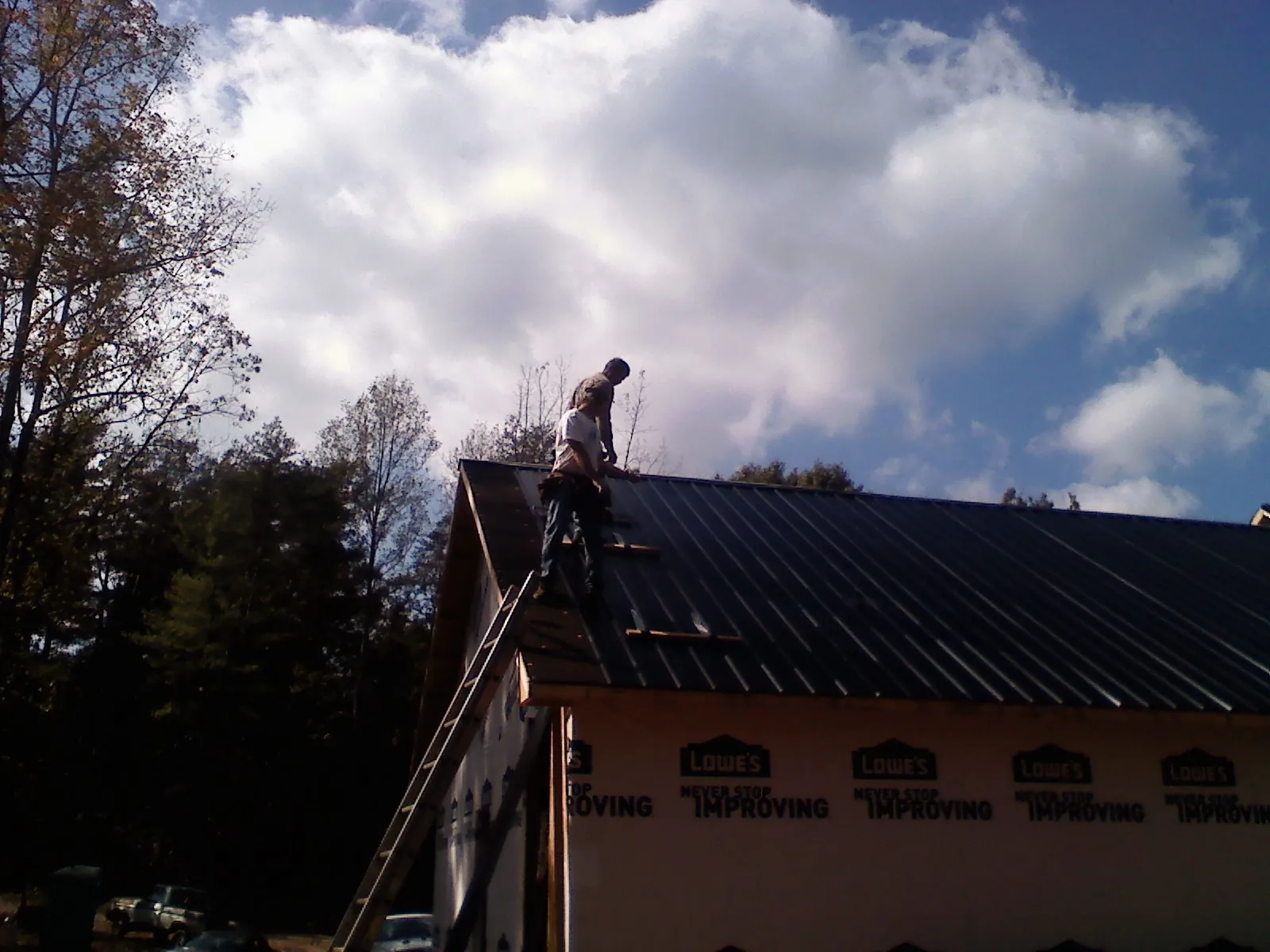 Roofer fastening dark metal panels high against a cloudy sky, from a Roof Inspection job in Ida